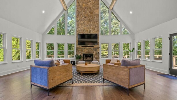 A spacious living room with high ceilings, large windows, and a stone fireplace. - Luxury Home w/Private Dock and Pool (Gainesville)