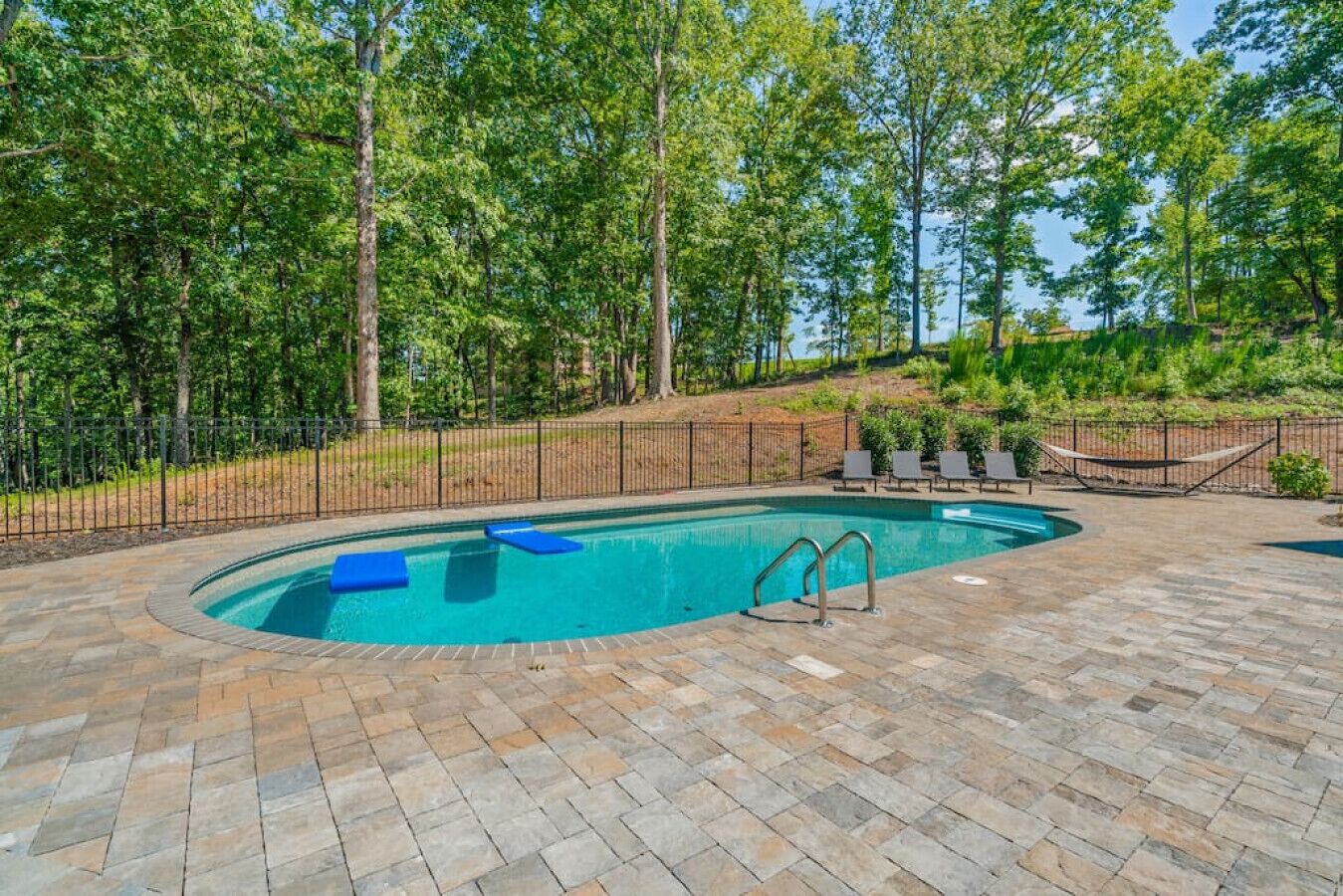 A swimming pool with a stone deck, surrounded by a fence and trees.