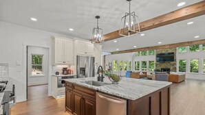 A spacious kitchen with a large island, wooden cabinets, and a stone fireplace. - Luxury Home w/Private Dock and Pool (Gainesville)