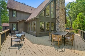 Une terrasse avec une table et des chaises, un pilier en pierre, et une maison dotée de grandes fenêtres et d’un toit en pente.