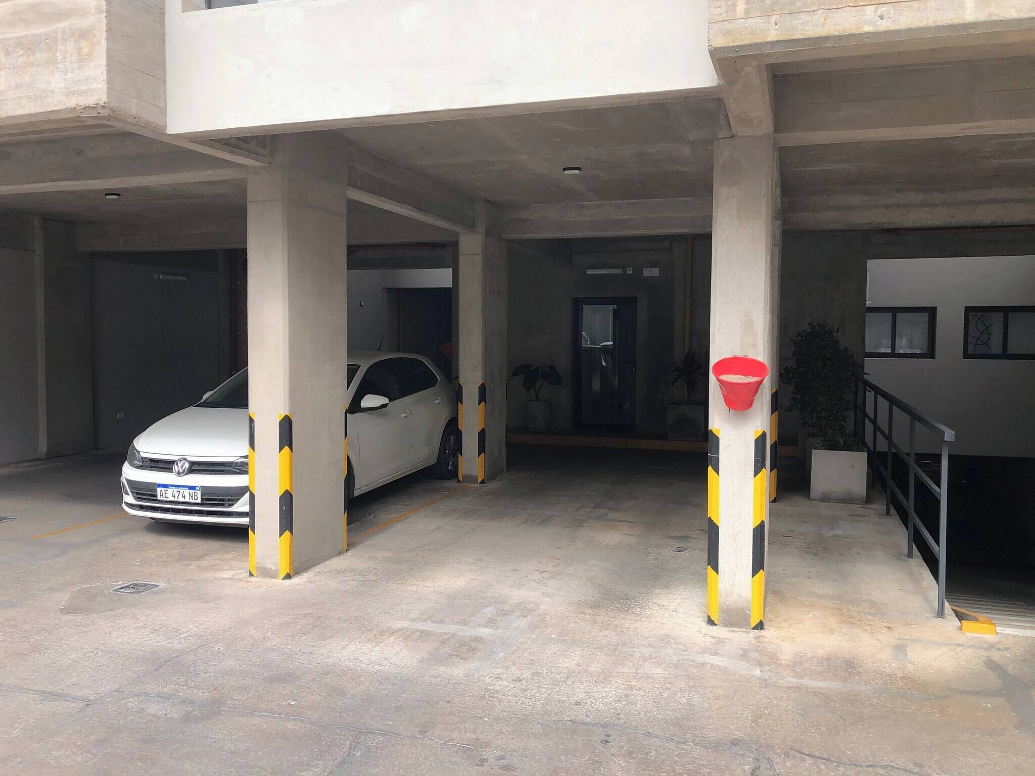 Un parcheggio con pilastri in cemento, un'auto bianca e un secchio rosso su un pilastro.
