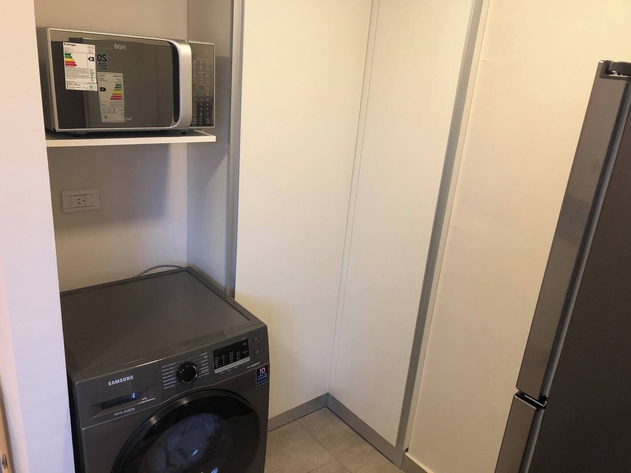 A laundry room with a washing machine, a microwave, and a refrigerator.