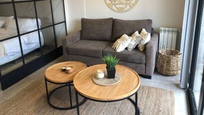 A modern living room with a sofa, two round wooden tables, a potted plant, and a decorative wall piece. - Apartment First Flor Excellent Location (Salta)
