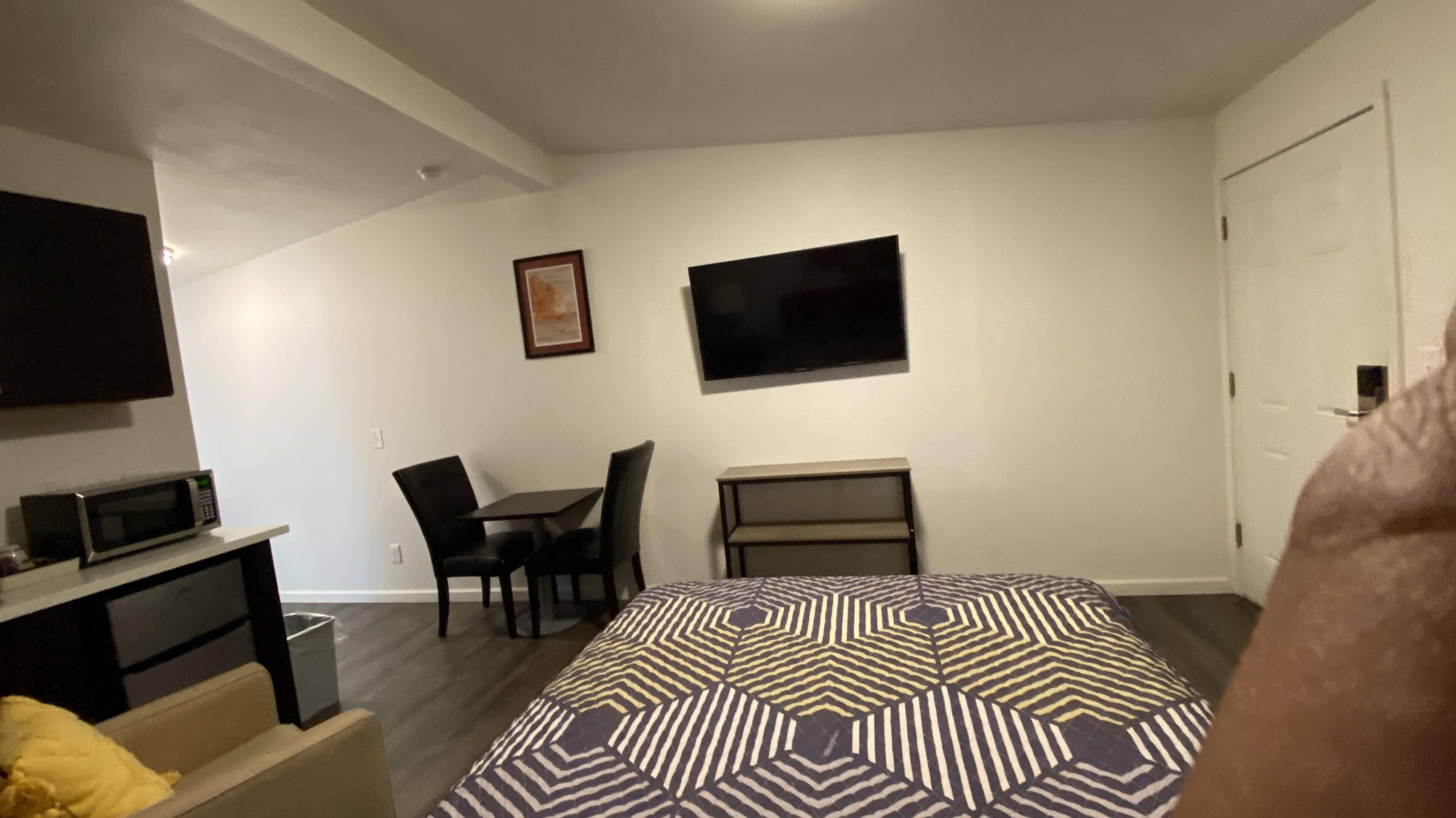 A compact hotel room with a bed, a desk, a chair, a TV, and a microwave.