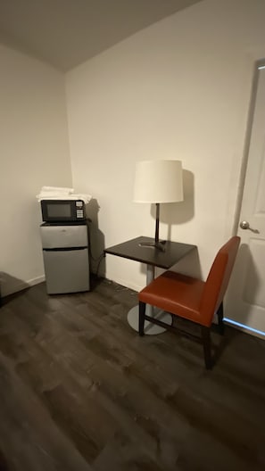 A compact room with a microwave on a small fridge, a table with a lamp, and a single chair. - Golden Kent Motel (Kent)