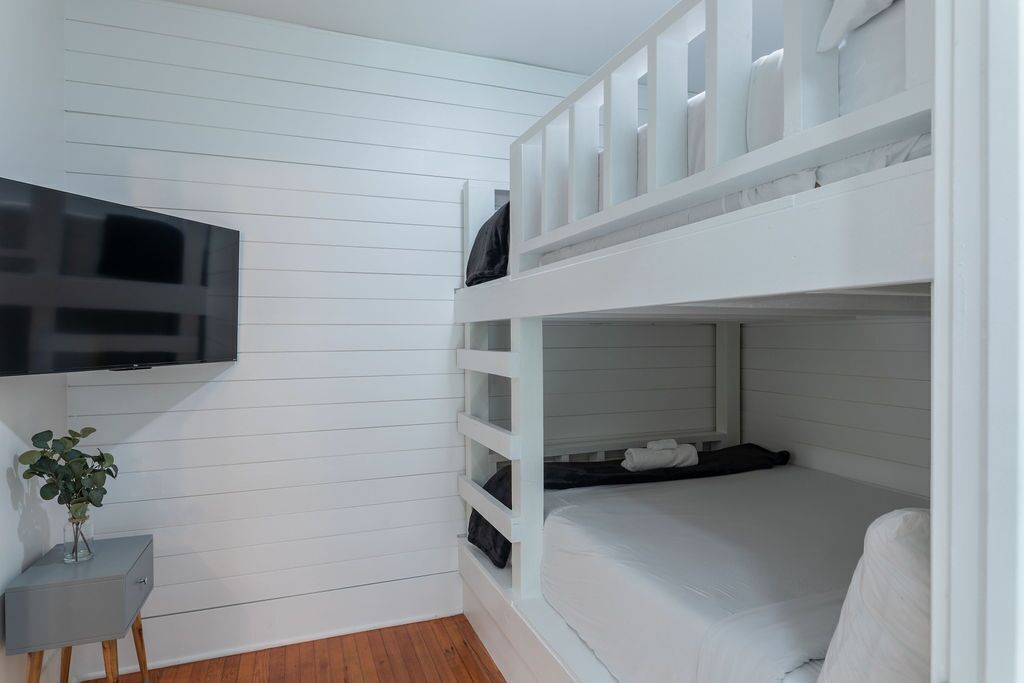 A bunk bed room with a TV on the wall, a small table with a plant, and a grey cabinet.