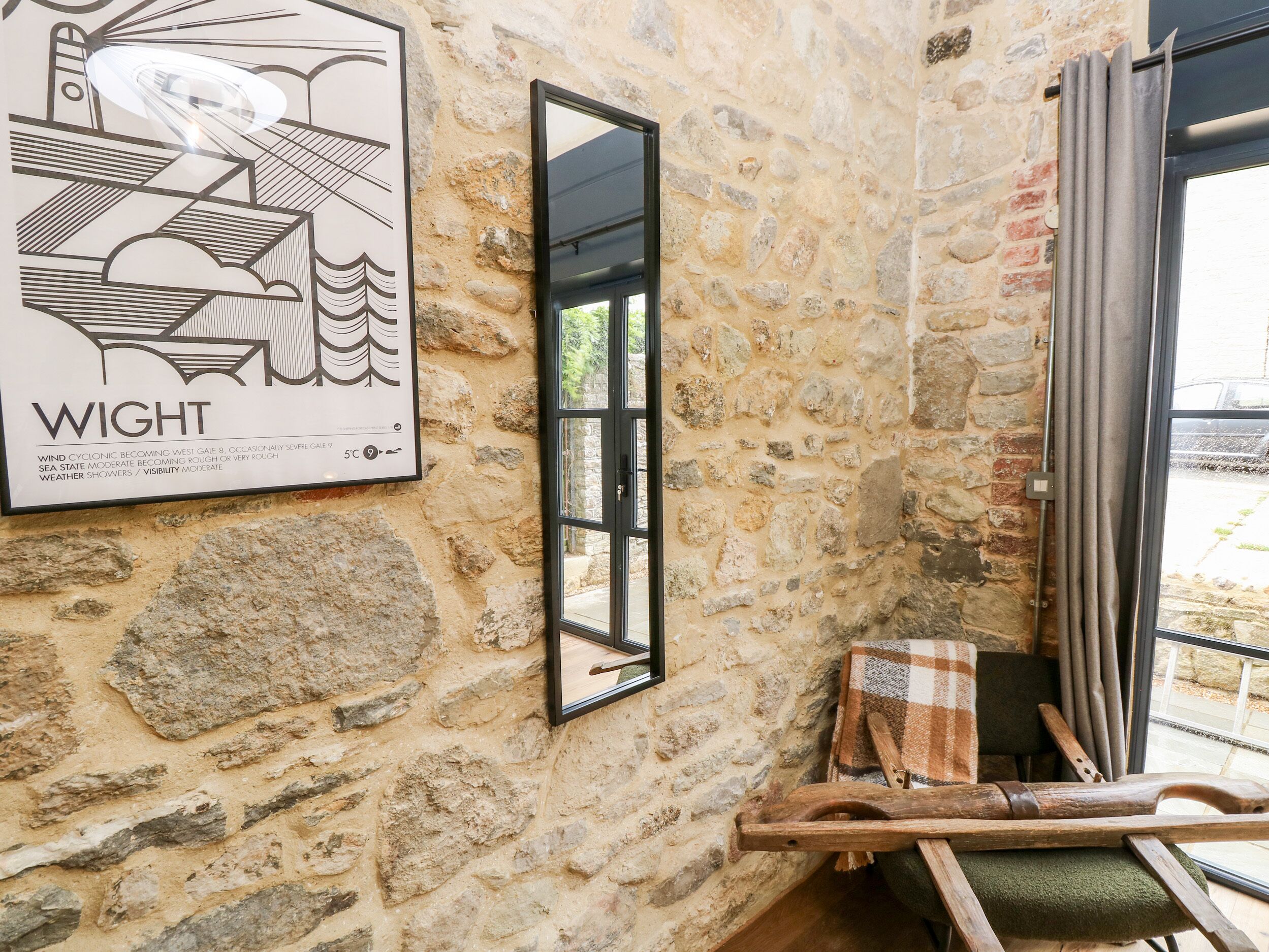 A stone-walled room with a framed weather map, a window, and a wooden bench.