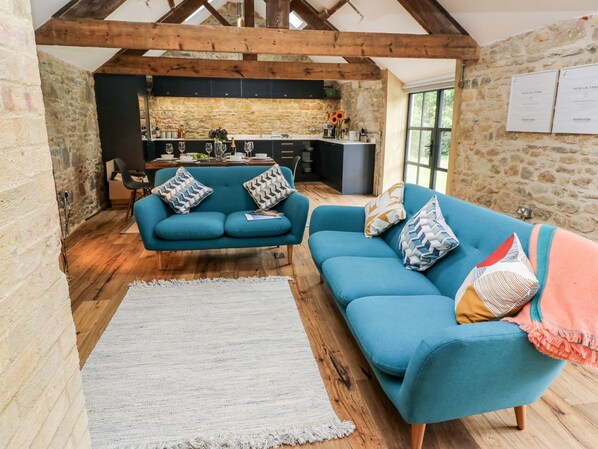 A cozy living room with a blue sofa set, a white rug, and a stone wall. - Tower Barn Cottage (Ryde)