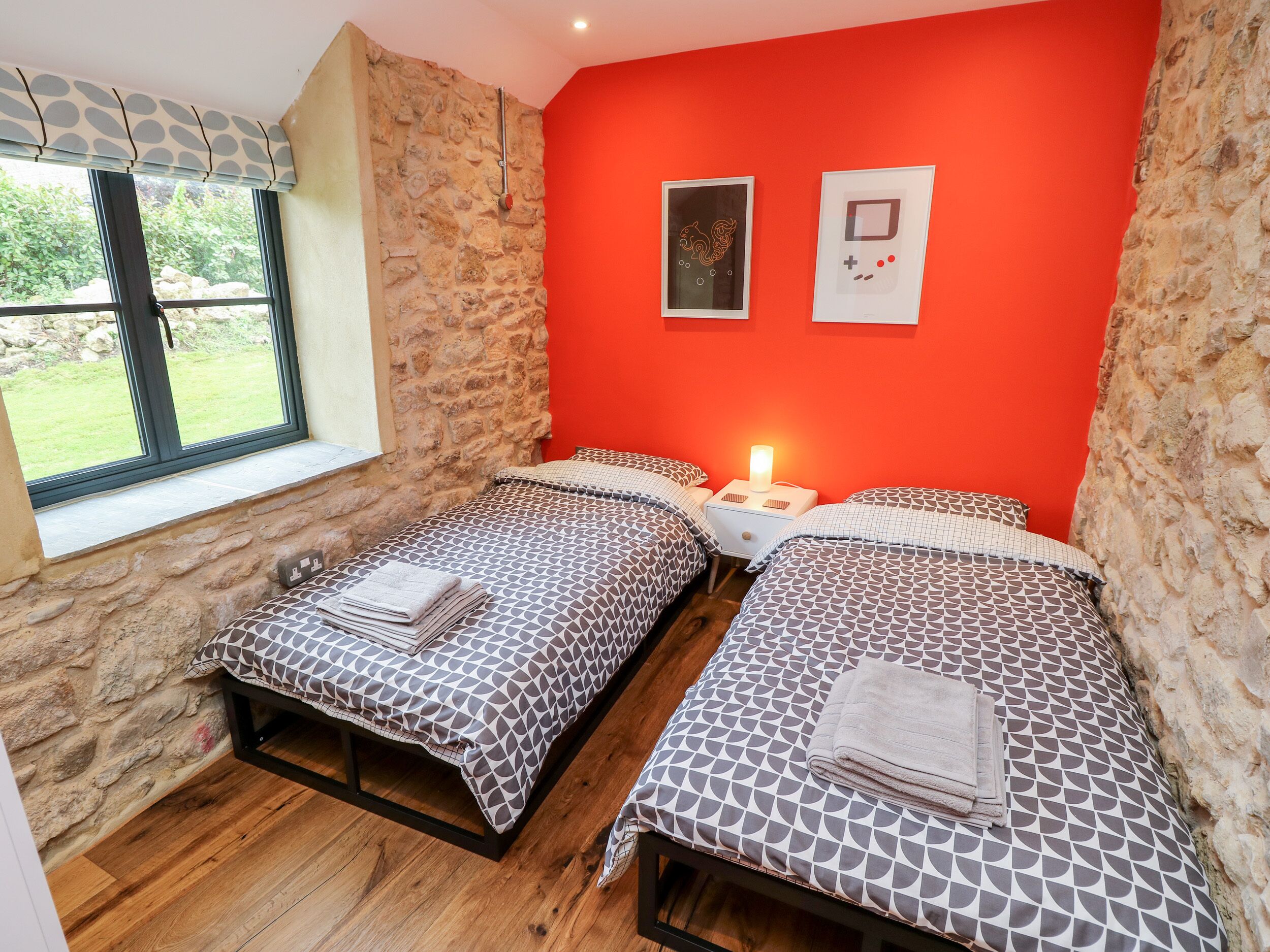 Un dormitorio con dos camas, una pared de piedra, una ventana con vistas y una pared roja con dos cuadros enmarcados.
