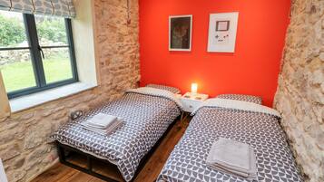Un dormitorio con dos camas, una pared de piedra, una ventana con vistas y una pared roja con dos cuadros enmarcados.