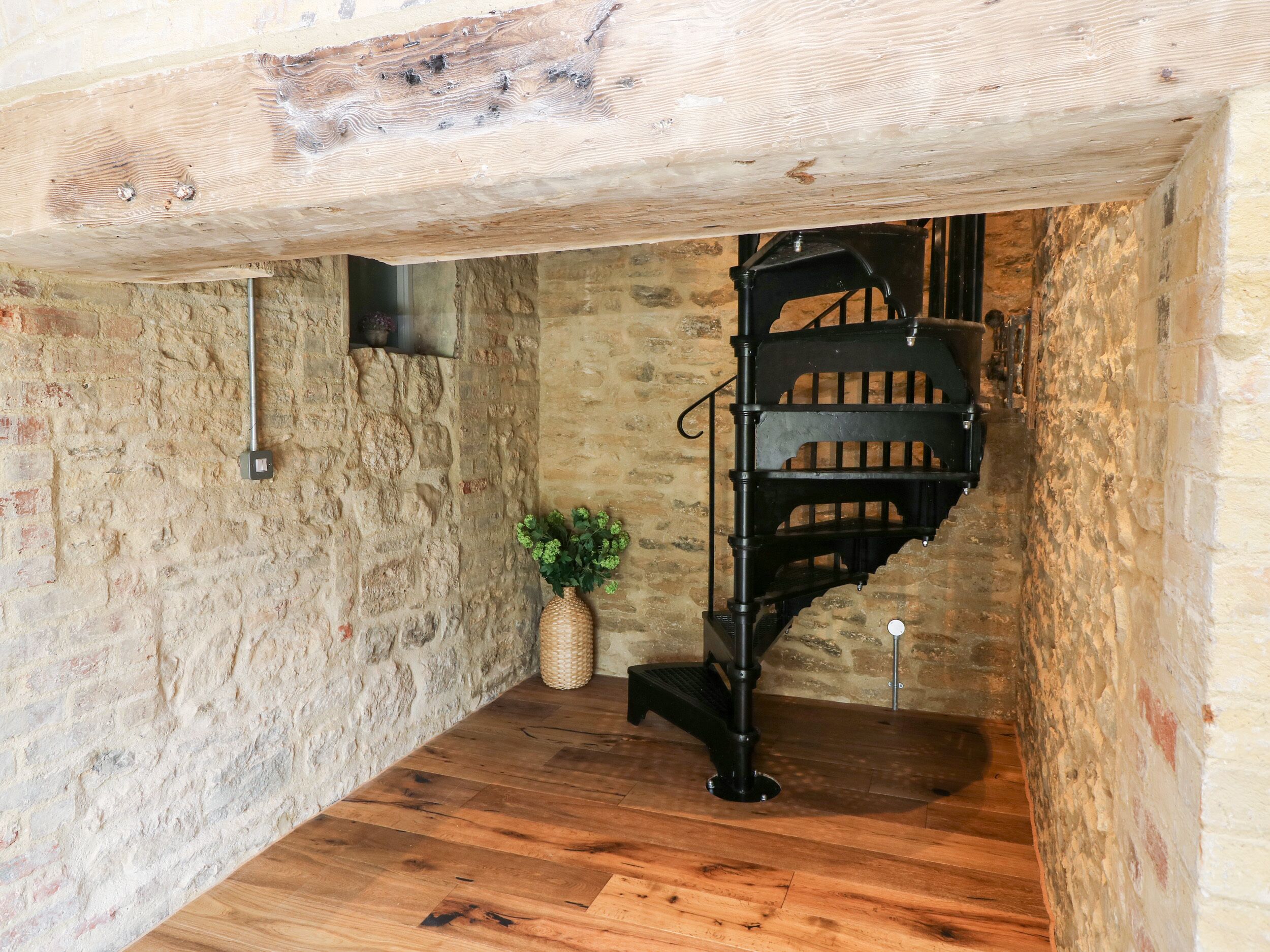 A rustic room with exposed stone walls, a wooden floor, and a black spiral staircase.
