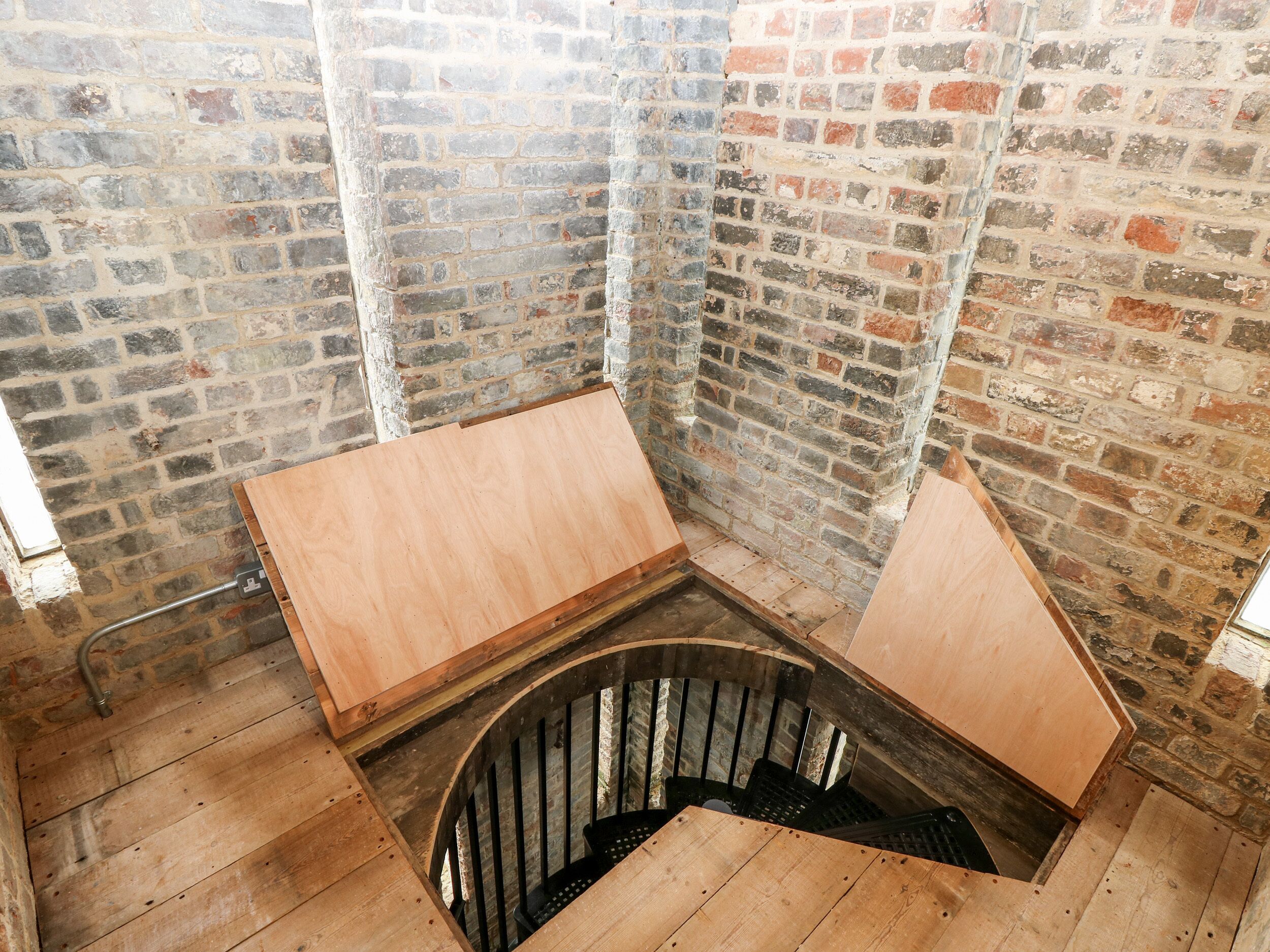 Ein Eckzimmer mit freiliegenden Backsteinwänden, Holzdielen und einer Wendeltreppe.