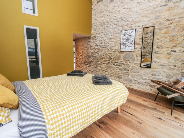 A bedroom with a checkered bedspread, a stone wall, and a framed artwork.