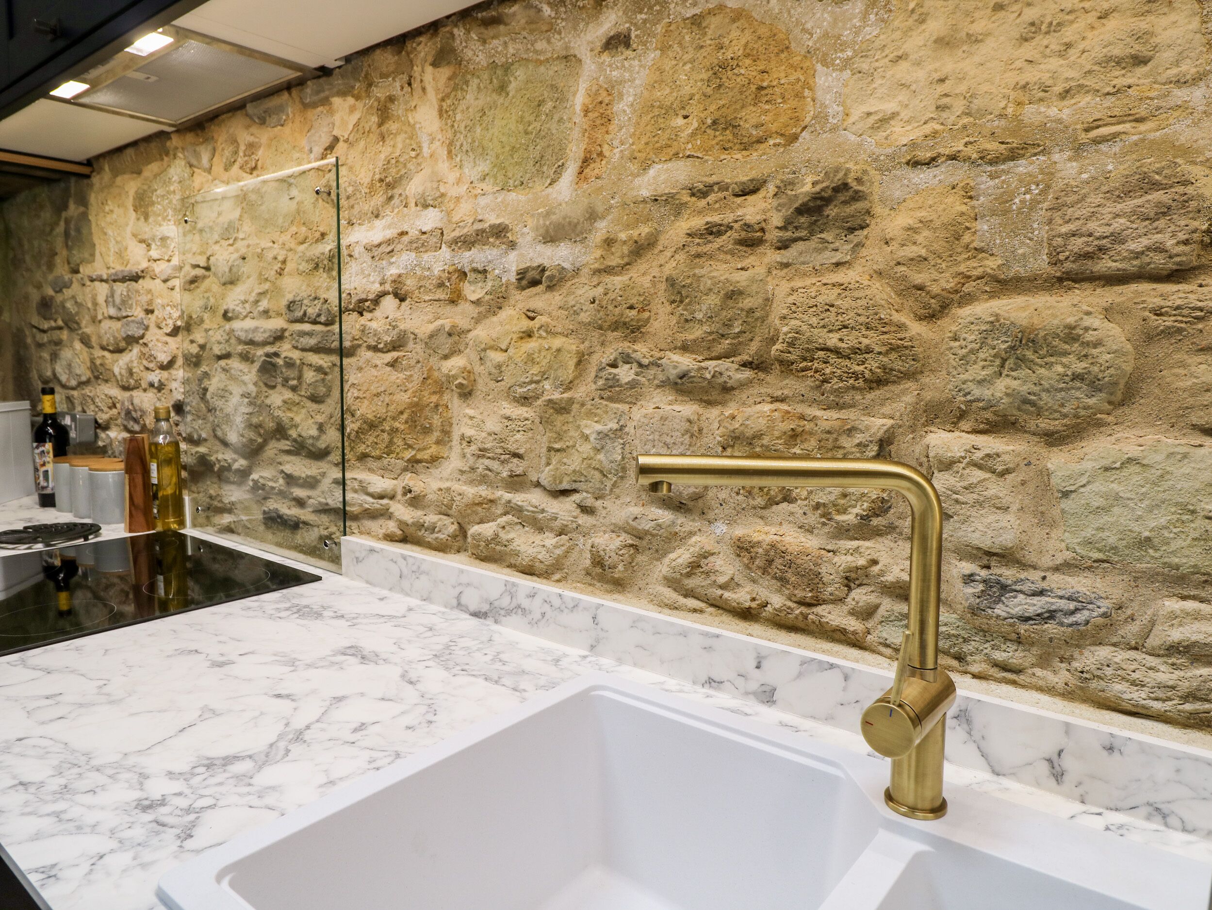 A bathroom with a stone wall, a marble sink, and a gold faucet.