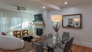 A modern living room with a glass dining table, comfortable seating, a fireplace, and a large mirror on the wall. - 💎 The Ares A Luxury! 💎 Montrose Bunker! 5BR ⭐️⭐️⭐️⭐️⭐️  (Houston)