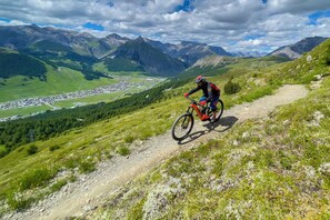 A mountain biker on a dirt trail with a town and mountains in the background.