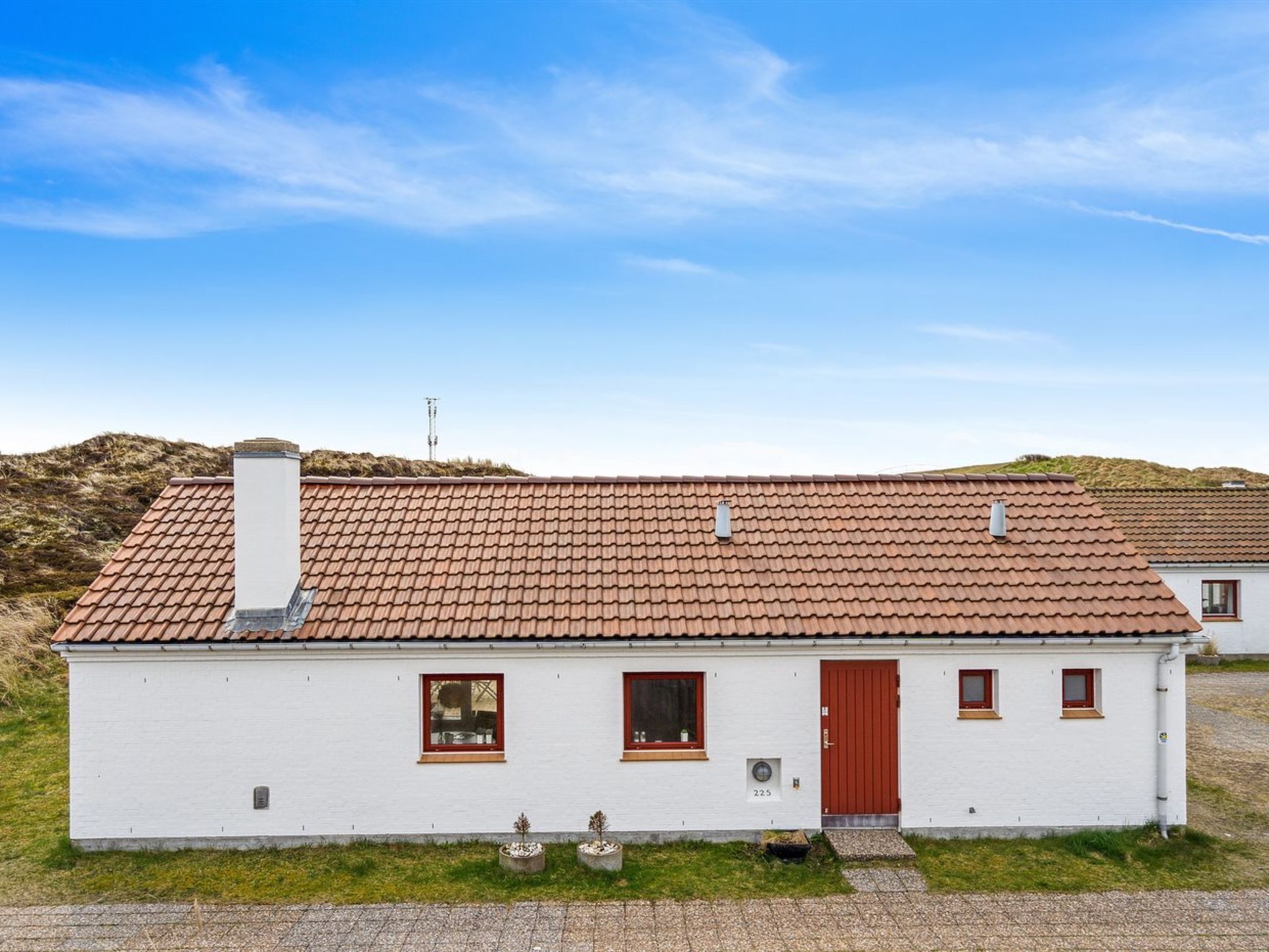 Een laag gebouw met witte muren, een rood pannendak, een rode deur en kleine ramen.