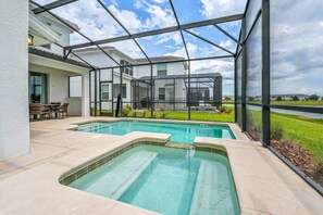 Une piscine entourée de parois en verre, un patio aménagé avec du mobilier d’extérieur, et une vue sur une maison en arrière-plan.