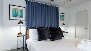 A hotel room with a large bed, two bedside tables with lamps, a ceiling fan, and artwork on the walls.
