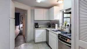 A compact kitchen with white cabinets, a stove, and a sink.