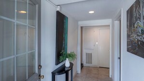 A hallway with a glass door, a black console table with a white vase and plant, and a large abstract painting on the wall.