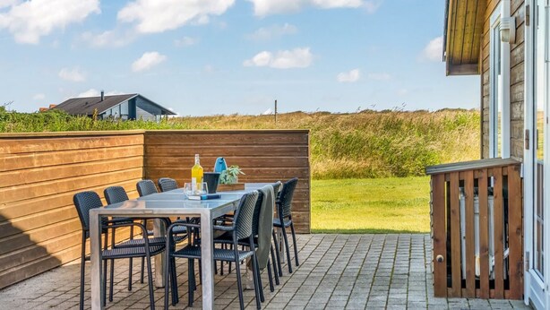 Une terrasse extérieure avec une table et des chaises, une clôture en bois et une pelouse, avec un bâtiment visible à l’arrière-plan.