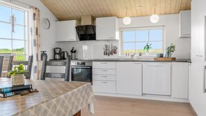 Une cuisine moderne avec des meubles blancs, un four encastré et une fenêtre donnant sur un jardin.