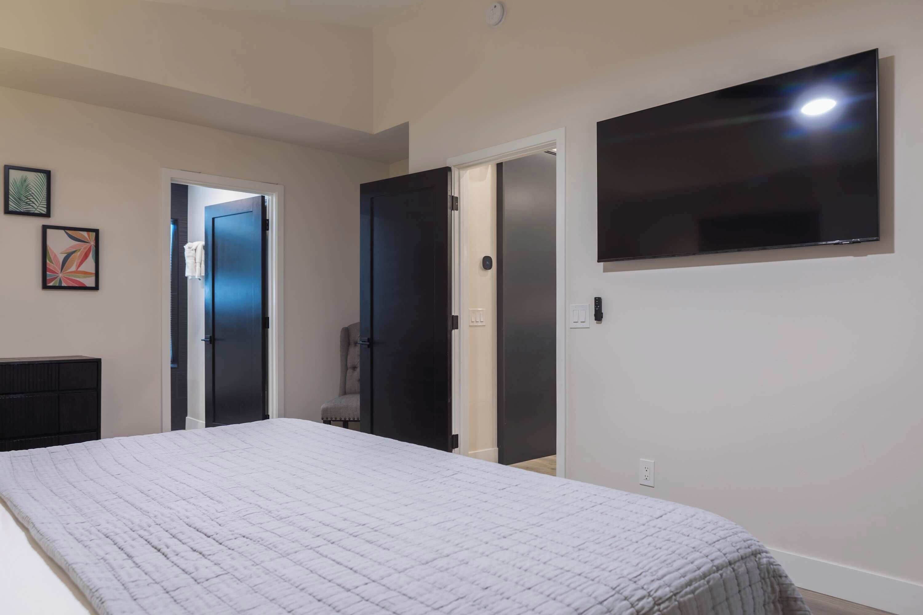 A bedroom with a bed, a TV mounted on the wall, and two doors leading to other rooms.