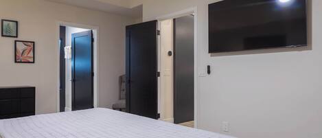 A bedroom with a bed, a TV mounted on the wall, and two doors leading to other rooms.