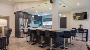 Een moderne keuken met een centraal eiland, barstoelen, roestvrijstalen apparatuur en hanglampen.