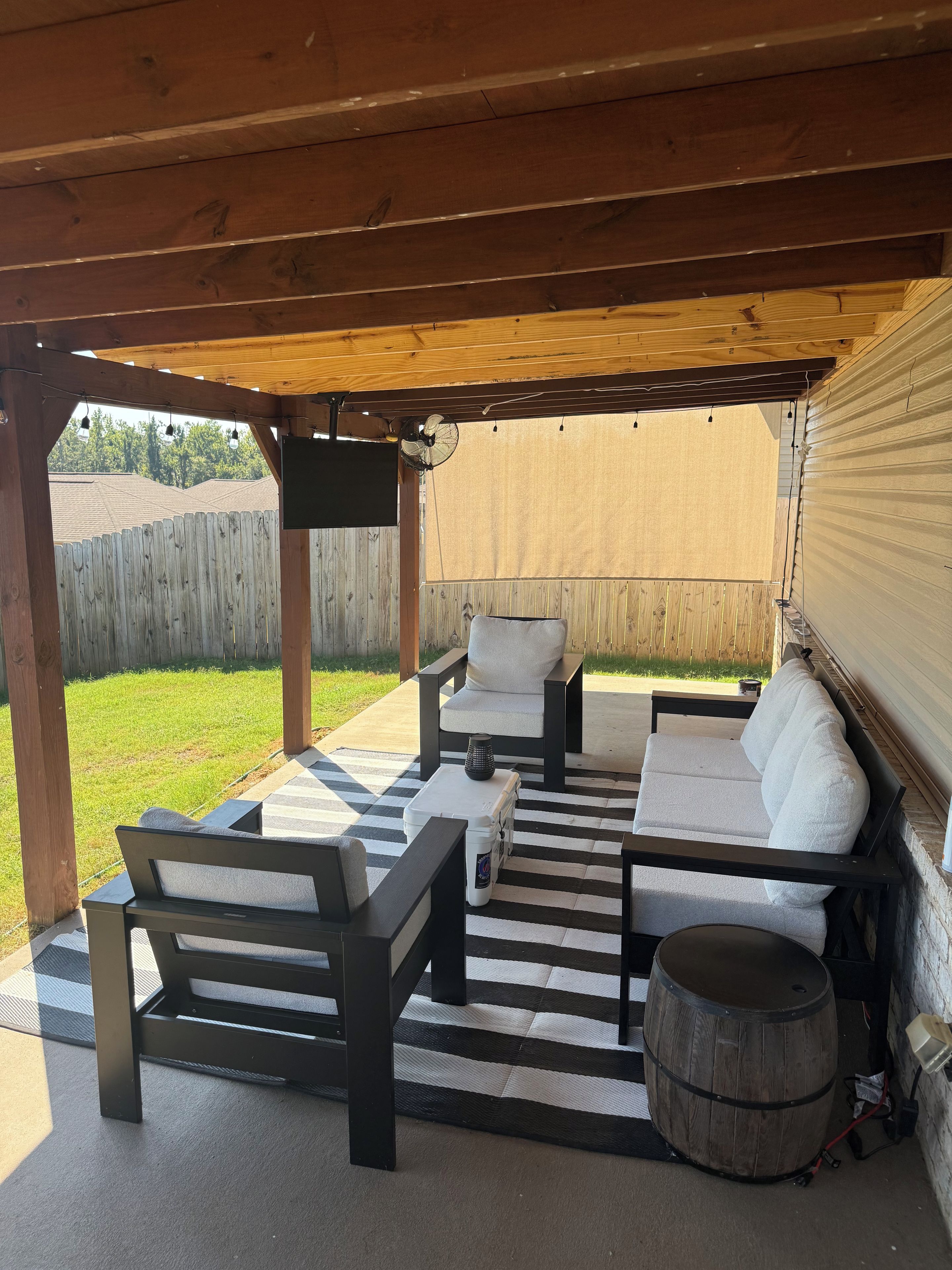 En utomhusplats med en träpergola, en soffgrupp, ett soffbord och en tunna.