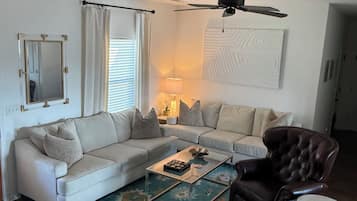 Ein Wohnzimmer mit Sofa, Sessel, Couchtisch und Deckenventilator.