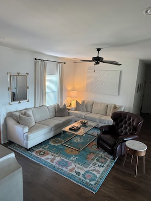 Una sala de estar con sofá, sillón, mesa de centro y ventilador de techo.