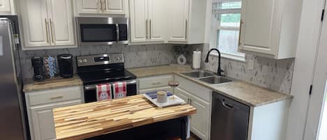 A kitchen with white cabinets, stainless steel appliances, a wooden bar counter, and a pet area.