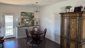 Un coin repas avec une table en bois, des chaises et un lustre. On y trouve également un meuble contenant des objets décoratifs et un tableau accroché au mur.