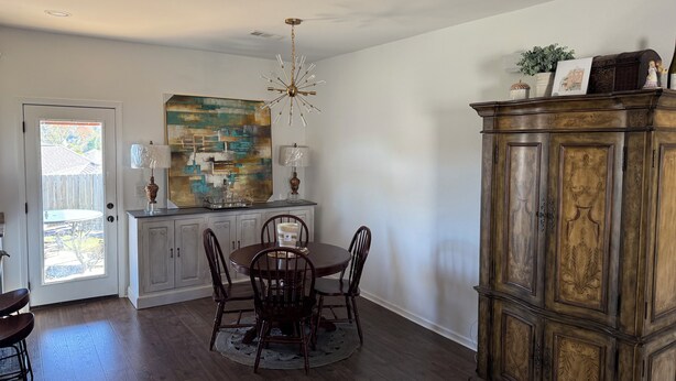 A dining area with a wooden table, chairs, and a chandelier. There is a cabinet with decorative items and a painting on the wall. - North Lamar hideout  (Oxford)