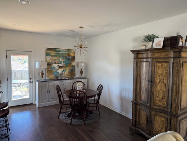 A dining area with a wooden table, chairs, and a chandelier. There is a cabinet with decorative items and a painting on the wall. - North Lamar hideout  (Oxford)