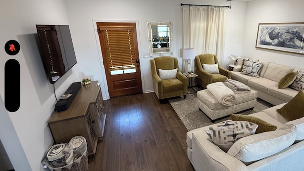 Un salon comprenant un canapé, des fauteuils, une table basse, un téléviseur, une porte avec des stores, un miroir et un tableau encadré accroché au mur.