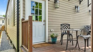 A wooden deck with a white door, a small table with chairs, and a potted plant.