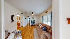 A spacious living room with a wooden floor, a brown leather sofa, a patterned armchair, and a television in the center.