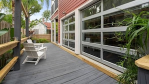 A wooden deck with white chairs, a red building with large windows, and a wooden fence. - Whitefish Lodge  Downtown Walk to Everything (St. Augustine)
