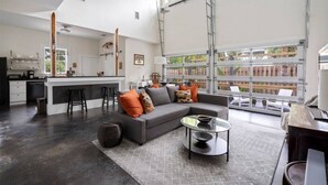 A spacious living area with a grey sofa, a coffee table, and a kitchen area with a bar and stools. - Whitefish Lodge  Downtown Walk to Everything (St. Augustine)