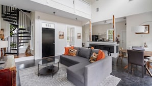 A modern living room with a grey sofa, black and orange cushions, a glass coffee table, and a black spiral staircase. - Whitefish Lodge  Downtown Walk to Everything (St. Augustine)