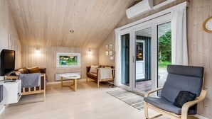 A cozy cabin interior with a wooden ceiling, a television, a dining table, and a comfortable seating area with a chair and sofa.