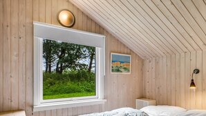 A bedroom with a large window, a bed, a bedside table, a radiator, and a wall-mounted lamp.