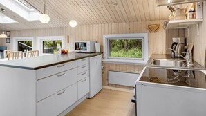 A modern kitchen with wooden ceiling, white cabinetry, a large island, and a window overlooking greenery.