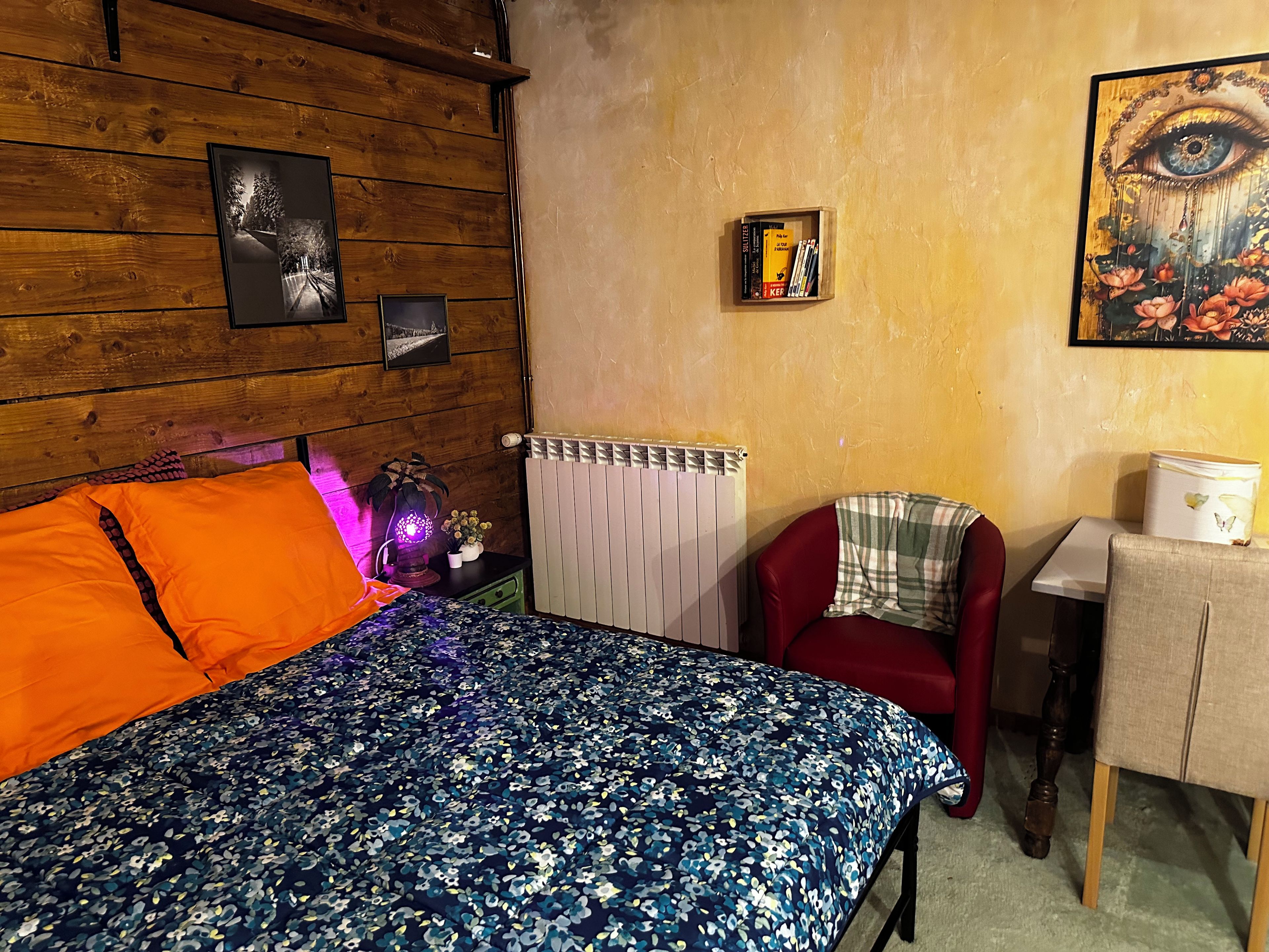Een kamer met een bed, een rode stoel, een radiator en een klein tafeltje met een lamp.