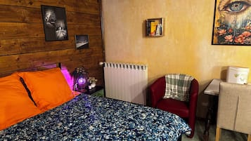 Een kamer met een bed, een rode stoel, een radiator en een klein tafeltje met een lamp.