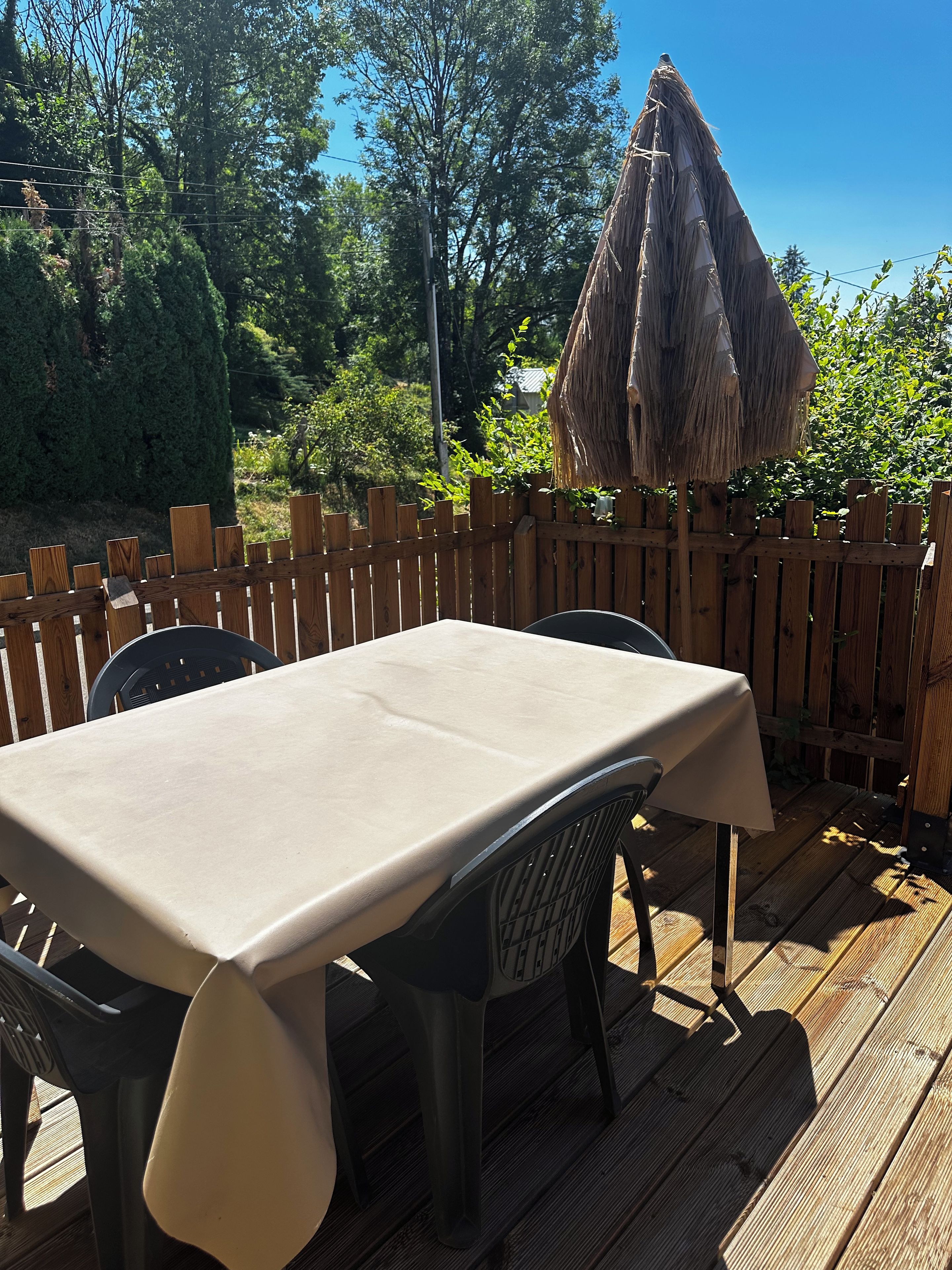 An outdoor wooden deck with a table and chairs, surrounded by a wooden fence and trees.