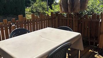 An outdoor wooden deck with a table and chairs, surrounded by a wooden fence and trees.